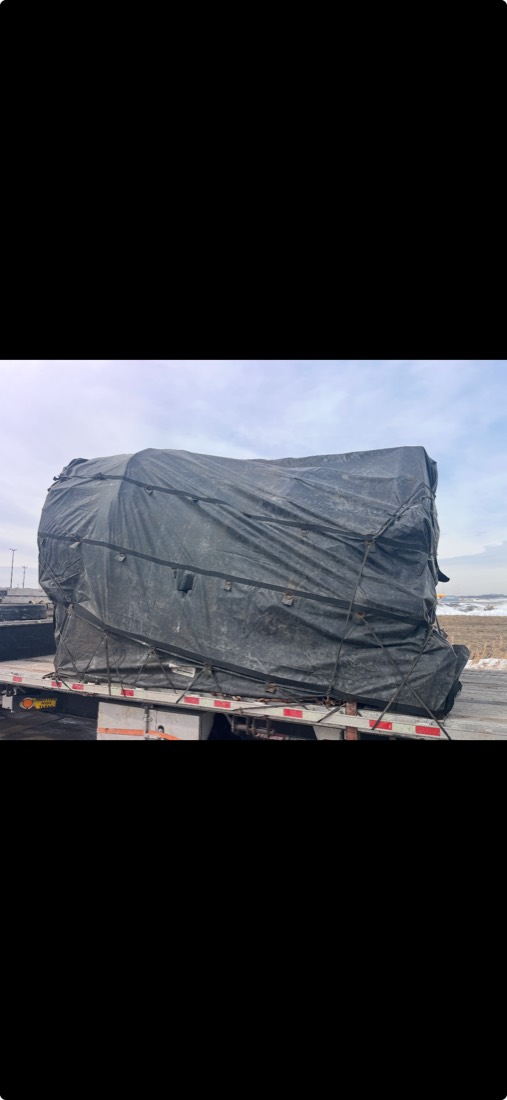 Same load covered with dark tarp and mesh netting, side view on flatdeck