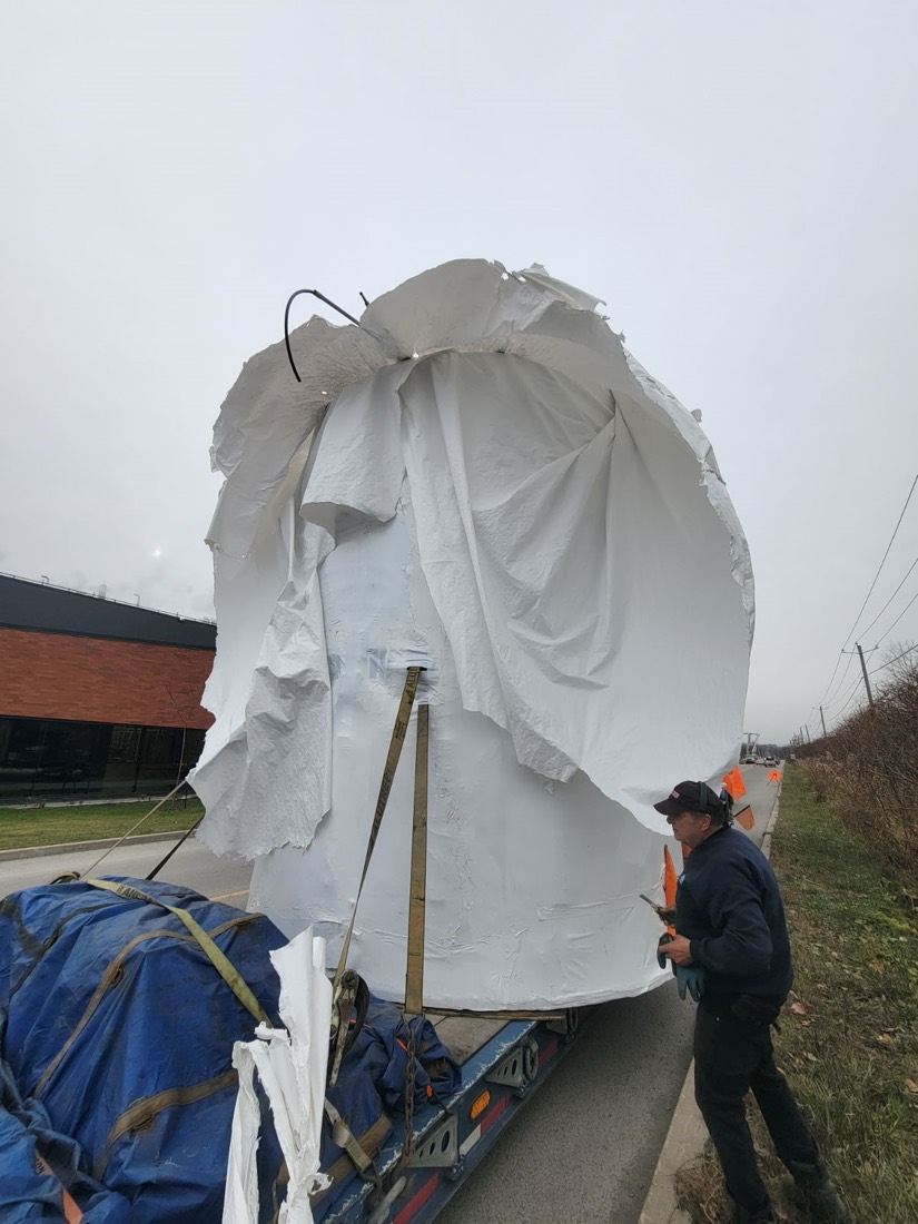 Trommel cage shrink-wrapped in white plastic with crew trimming excess at curbside