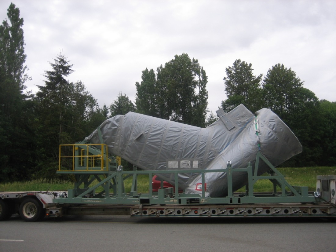Shrink-wrapped aircraft tail section with engine housing cradled on green steel rack