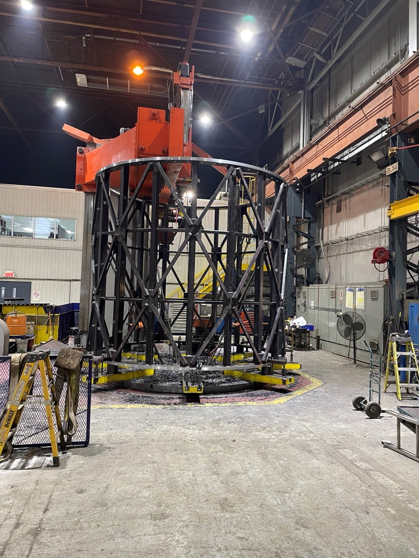 Trommel cage on rotating turntable inside fab shop, orange overhead jib above