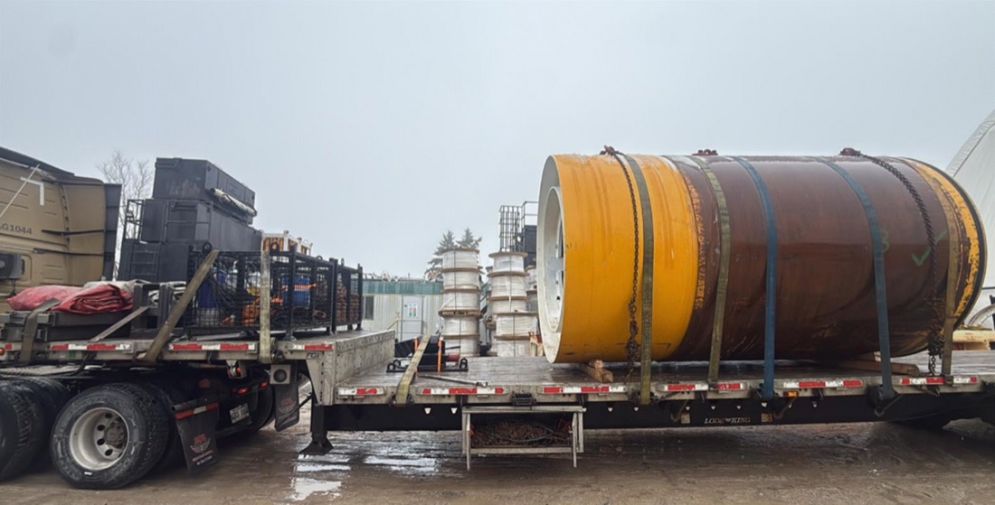 Yellow steel-banded TBM tunnel liner / precast cylinder strapped to flatdeck at fabricator yard