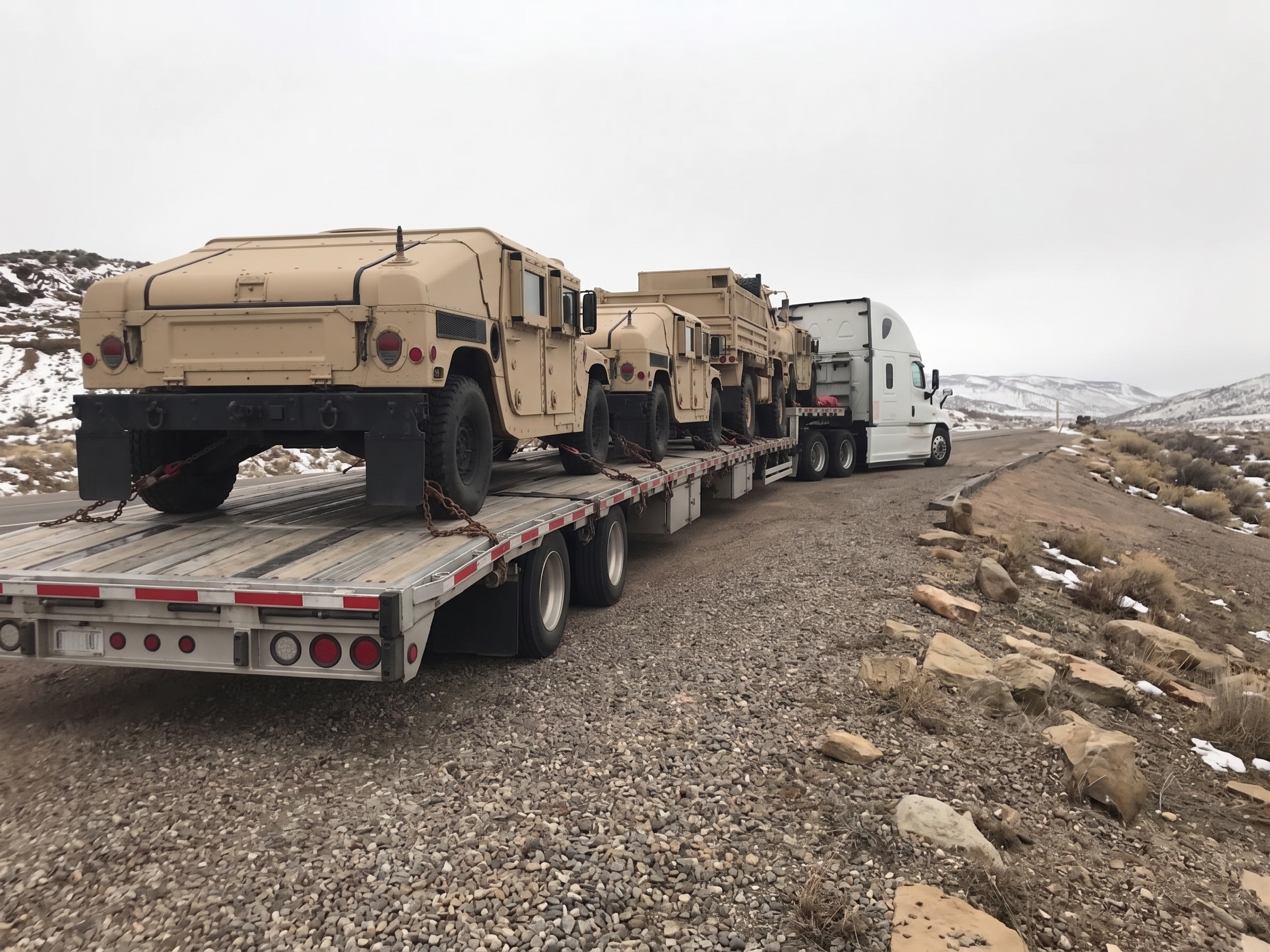 Rear view down the stepdeck — military Humvees and tactical truck chained for transport on a winter highway
