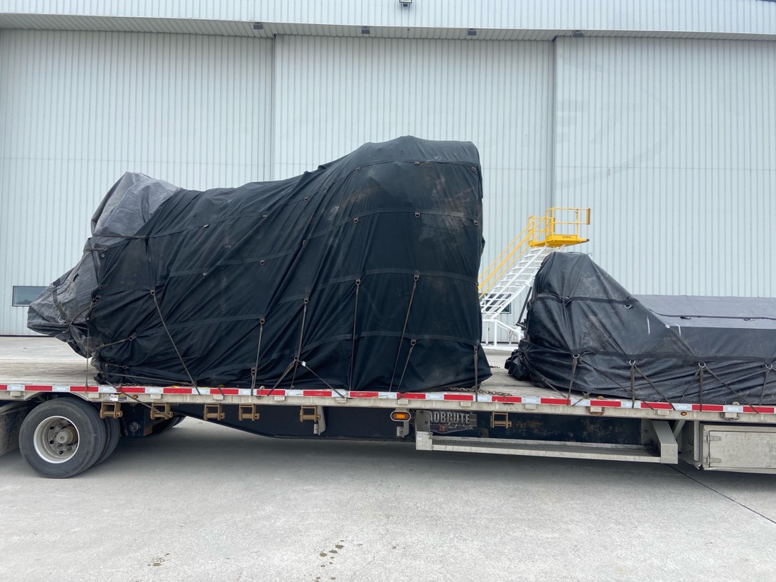 Two tarped & netted aero shipments on Roadbrute stepdeck at hangar with access stairs