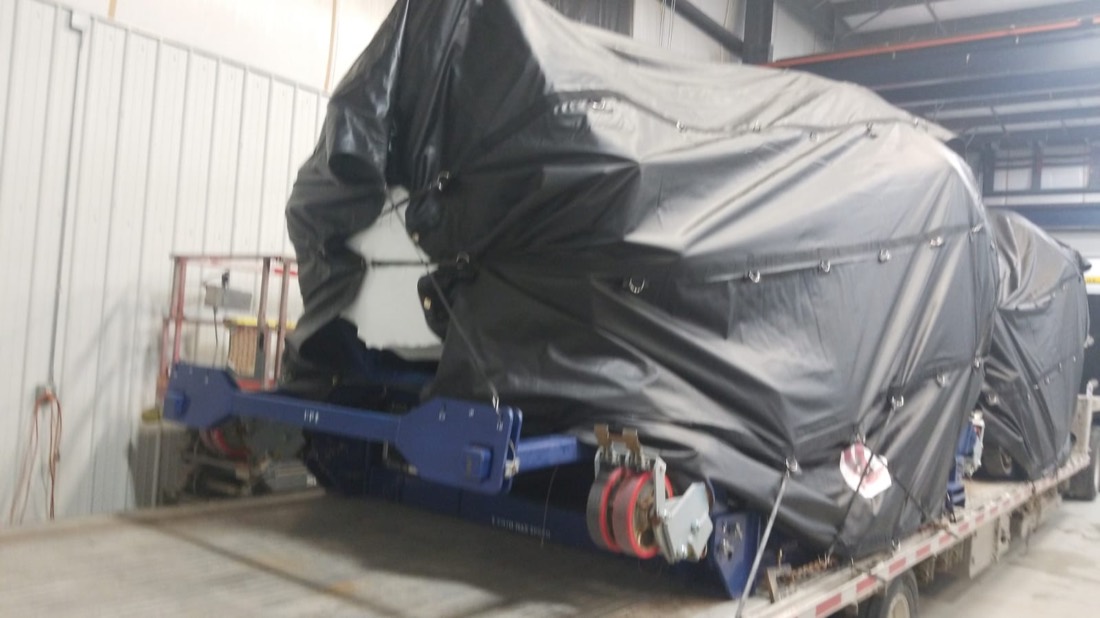 Aircraft component on blue Schreuder beam trailer being tarped inside fabrication shop