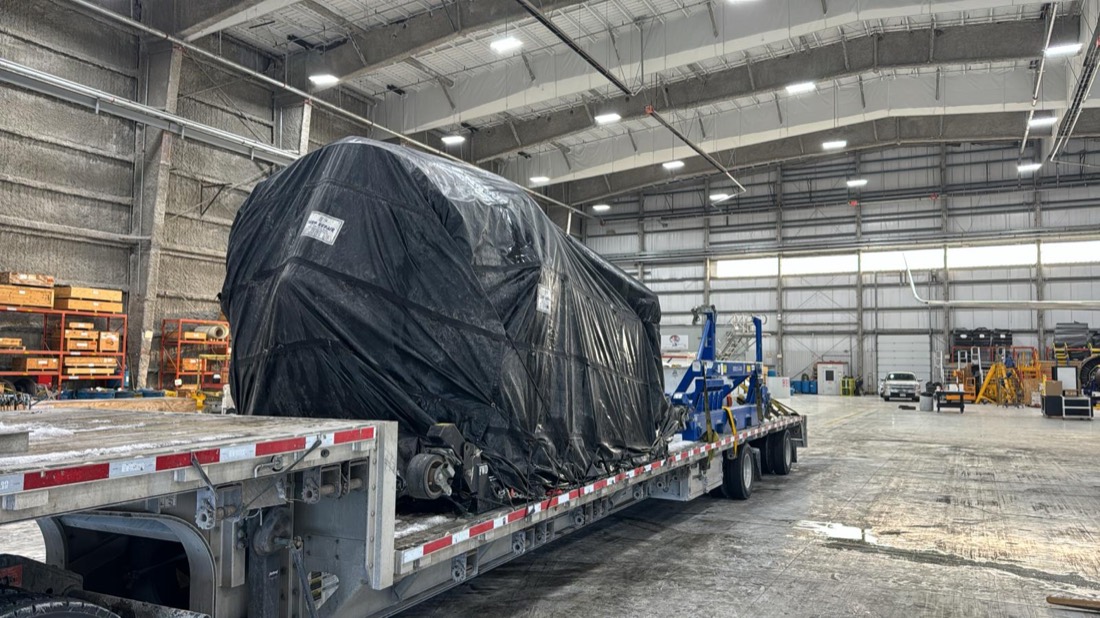 Black-tarped aero component on stepdeck inside hangar, prepared for road transport