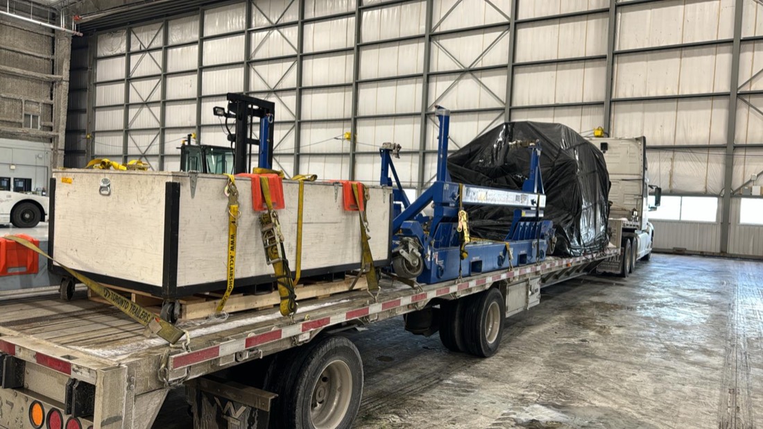 Forklift positioning wooden aero crate beside blue cradle and tarped load on stepdeck