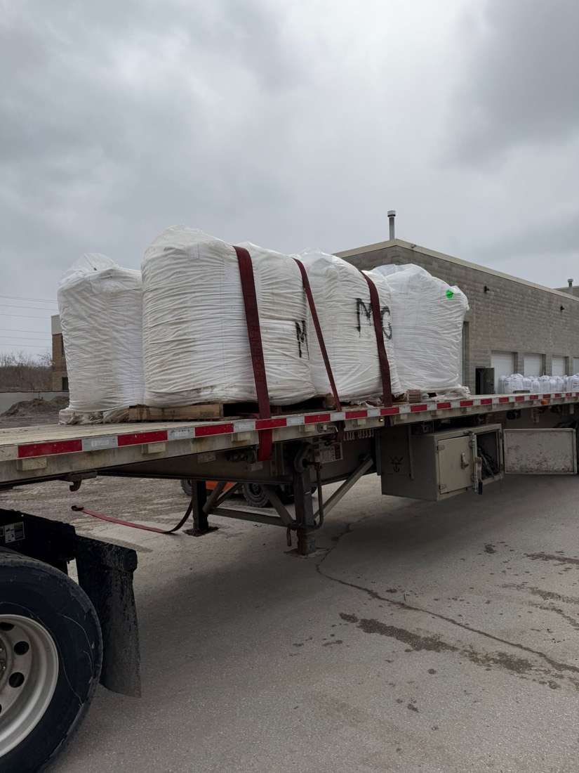Row of white FIBC bulk bags marked &ldquo;MG&rdquo; loaded on tridem flatdeck at warehouse