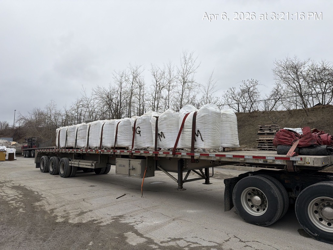 Tridem flatdeck with full row of FIBC bulk bags strapped down at yard, rear-quarter view