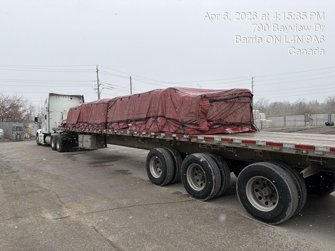 Side view of red-tarped tridem flatdeck load with day-cab tractor attached