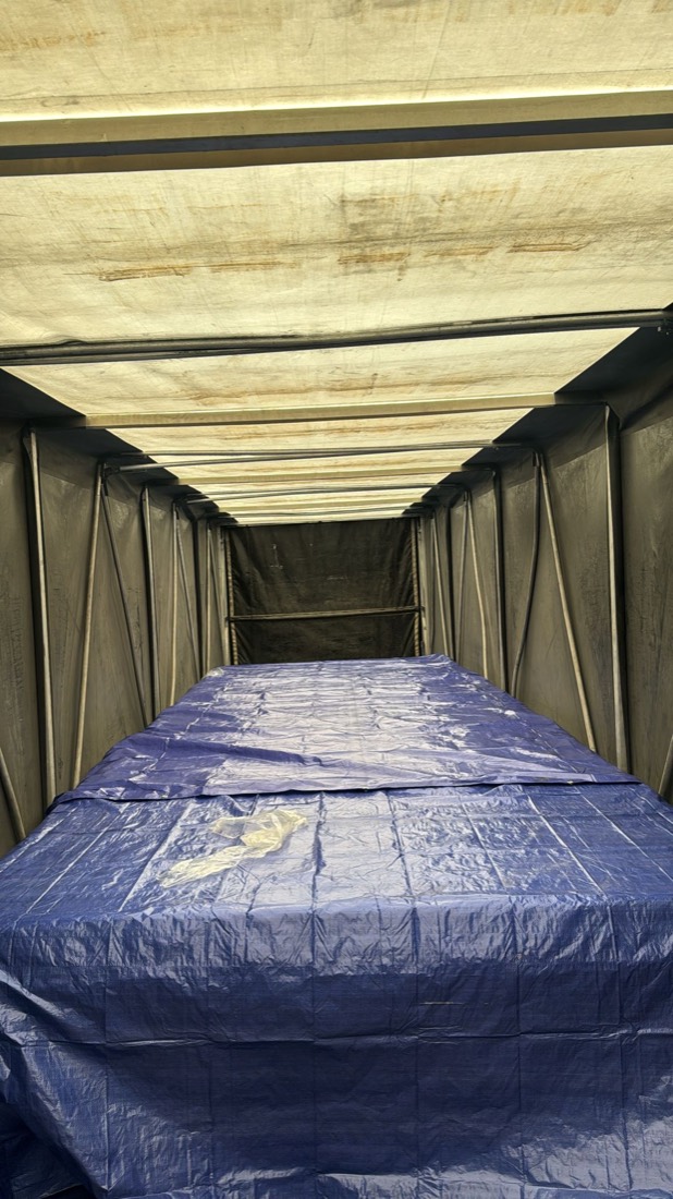 Interior of curtain trailer with blue tarp draped over flat load, ratchet straps overhead