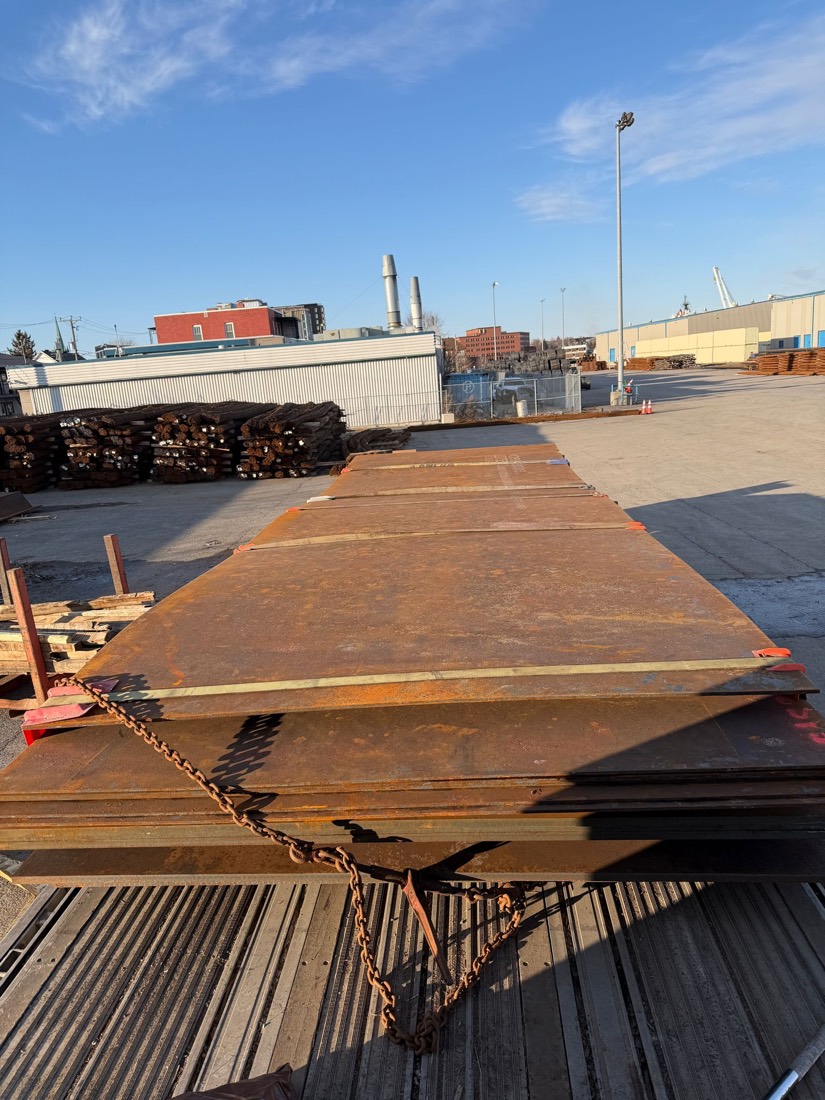 Bundles of rusty steel plate stacked & chained on flatdeck at industrial yard