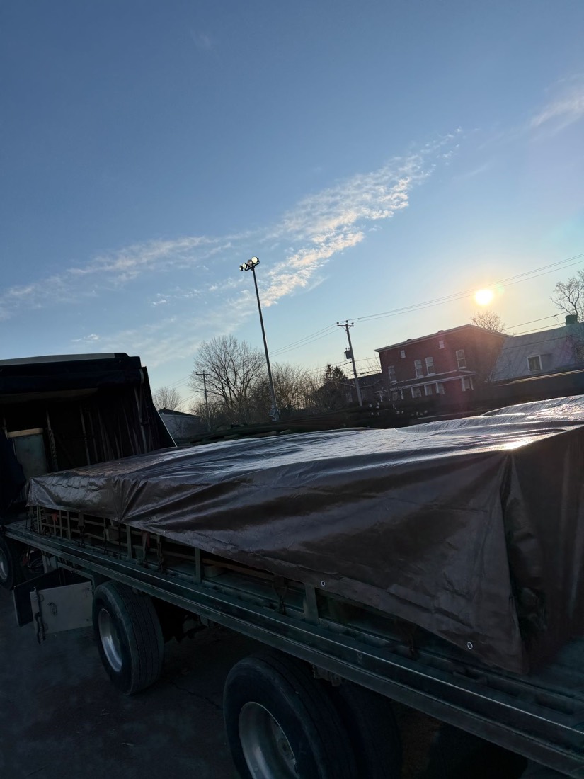 Long flatdeck with brown tarp cover at sunset, residential block in background