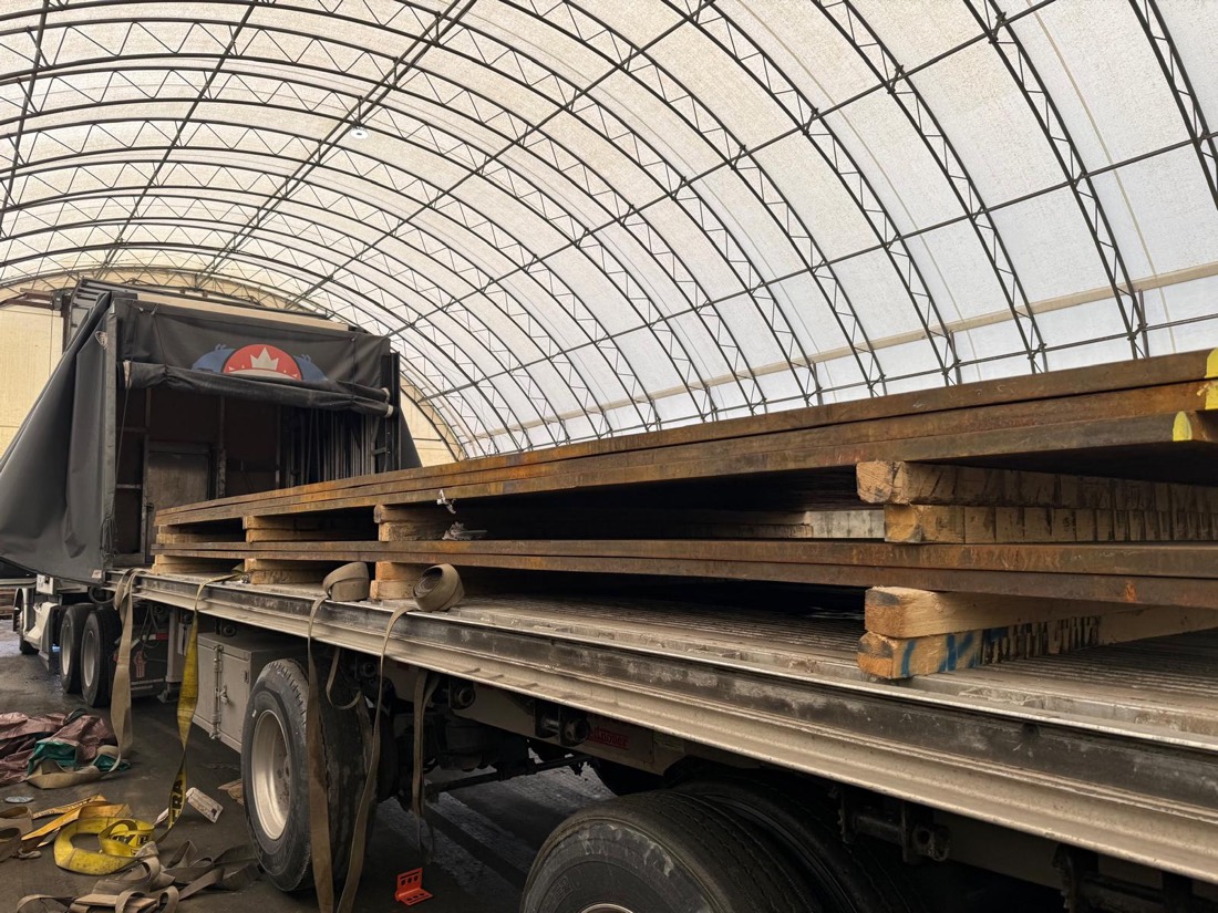 Steel plate load on flatdeck staged inside arched fabric storage shelter for tarping