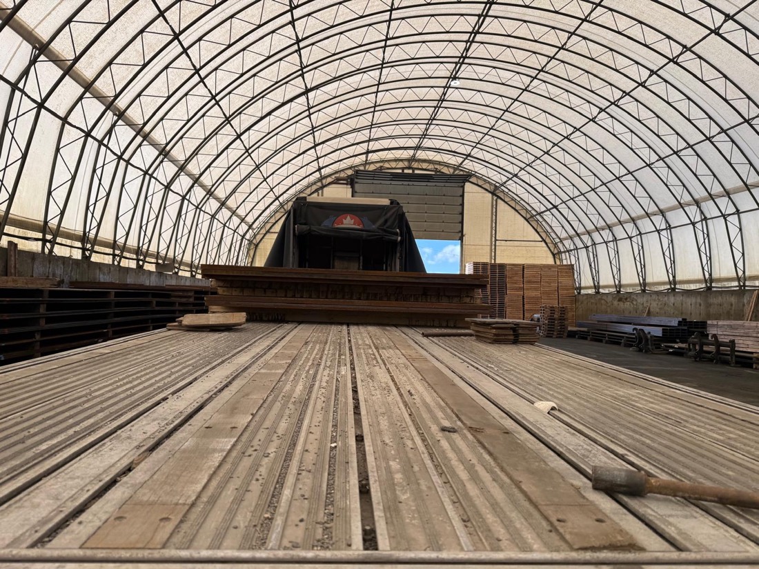 Empty flatdeck deck inside arched fabric shelter awaiting next plate stack load