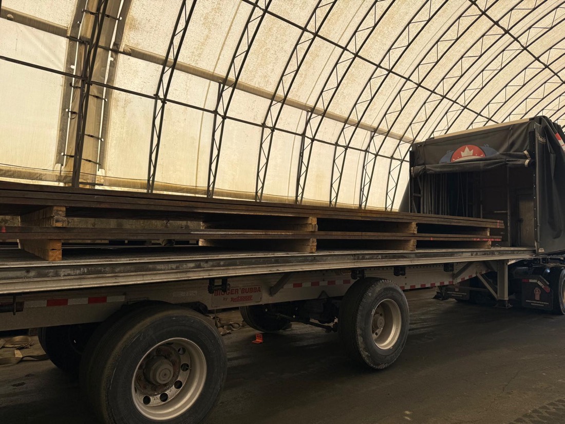 Bigger Bubba flatdeck with steel plate stacks loaded under fabric shelter, Canada flag on curtain